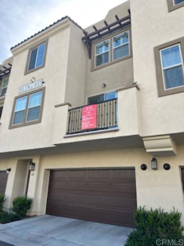 multi unit property featuring an attached garage, concrete driveway, a balcony, and stucco siding