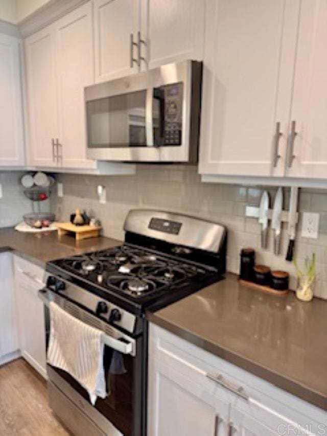 kitchen featuring white cabinets, light wood finished floors, dark countertops, decorative backsplash, and appliances with stainless steel finishes