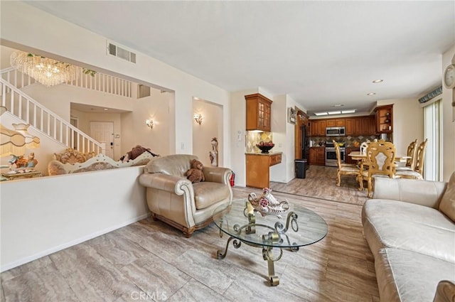living room with visible vents, light wood-type flooring, stairway, and an inviting chandelier