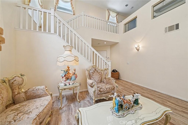 living area featuring stairs, baseboards, wood finished floors, a towering ceiling, and visible vents