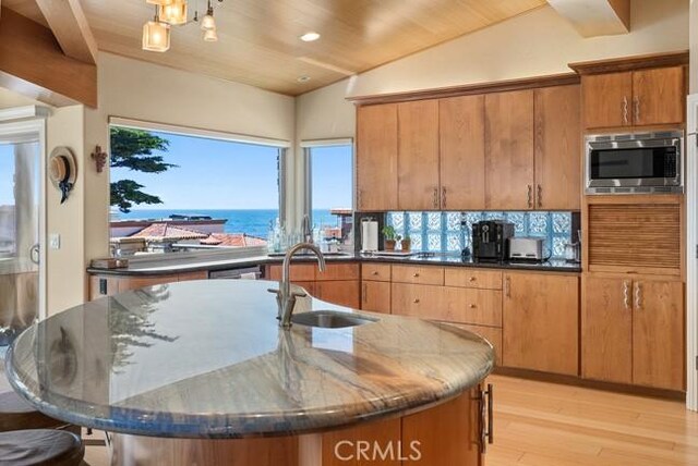 2062 Sherwood Dr, Cambria, CA 93428 - kitchen with a sink, stainless steel microwave, light wood-style flooring, dark stone counters, and backsplash