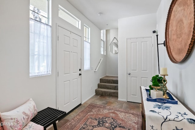 foyer entrance with baseboards, stone tile floors, and stairs