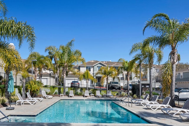 community pool with a patio, fence, and a residential view