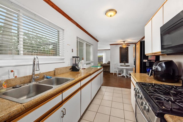 kitchen featuring a sink, black microwave, white cabinetry, light tile patterned floors, and stainless steel range with gas cooktop