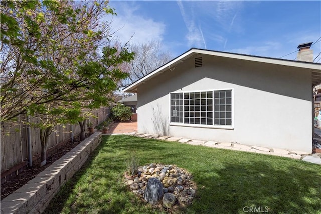 view of property exterior featuring stucco siding, a chimney, fence, and a yard