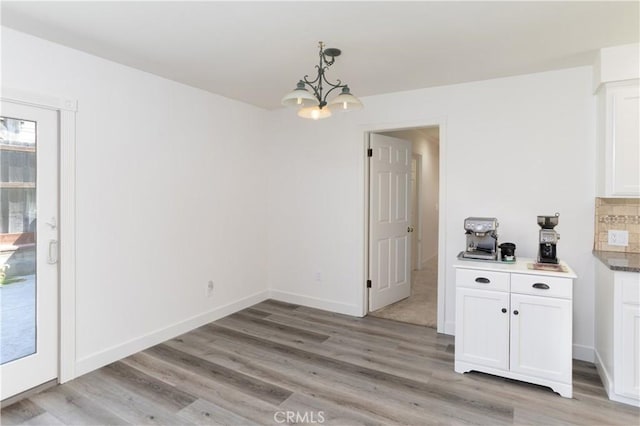 unfurnished dining area featuring an inviting chandelier, baseboards, and light wood-type flooring