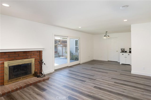 unfurnished living room with a brick fireplace, baseboards, and wood finished floors