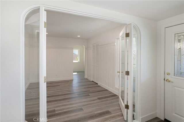 hall with french doors, arched walkways, baseboards, and wood finished floors