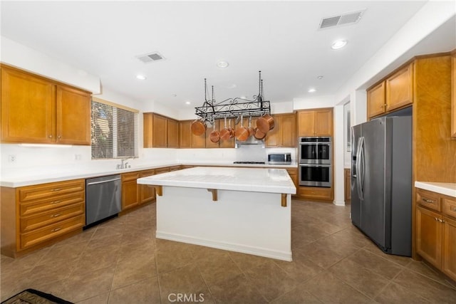 15686 Iron Spring Ln, Fontana, CA 92336 - kitchen with appliances with stainless steel finishes, a center island, brown cabinetry, light countertops, and recessed lighting