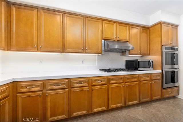 15686 Iron Spring Ln, Fontana, CA 92336 - kitchen with appliances with stainless steel finishes, under cabinet range hood, light countertops, and brown cabinets