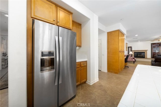 15686 Iron Spring Ln, Fontana, CA 92336 - kitchen featuring stainless steel fridge, tile countertops, open floor plan, light tile patterned floors, and a glass covered fireplace