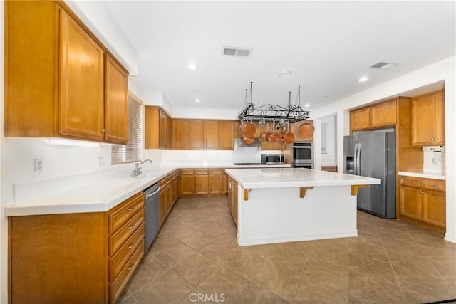 15686 Iron Spring Ln, Fontana, CA 92336 - kitchen featuring appliances with stainless steel finishes, a breakfast bar area, light countertops, a center island, and brown cabinetry