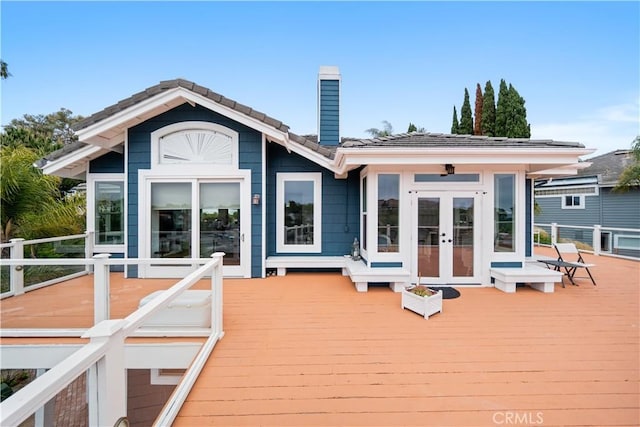 rear view of house with a tile roof, a wooden deck, a chimney, and french doors