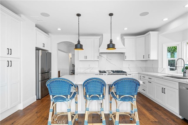 kitchen featuring a sink, appliances with stainless steel finishes, premium range hood, white cabinets, and arched walkways
