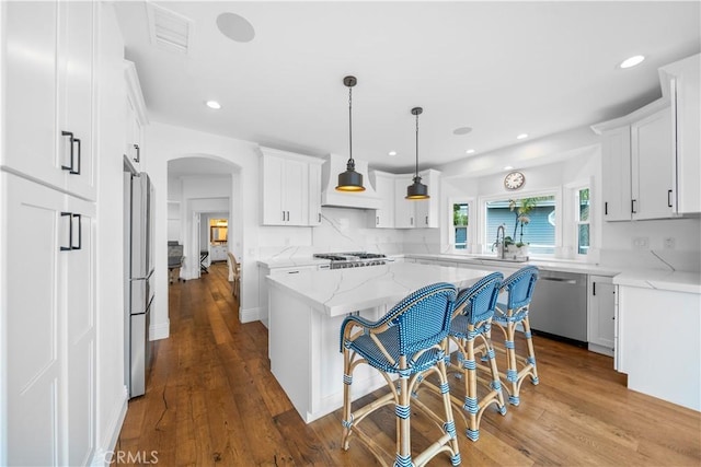 kitchen featuring backsplash, custom range hood, stainless steel appliances, visible vents, and arched walkways