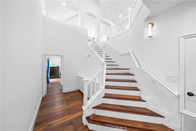 stairs with baseboards, wood finished floors, and a towering ceiling