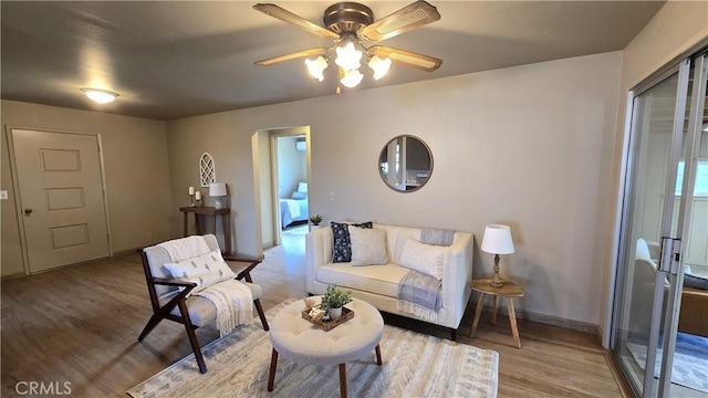 living area with baseboards, wood finished floors, and ceiling fan