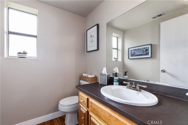 half bathroom featuring wood finished floors, visible vents, toilet, vanity, and baseboards