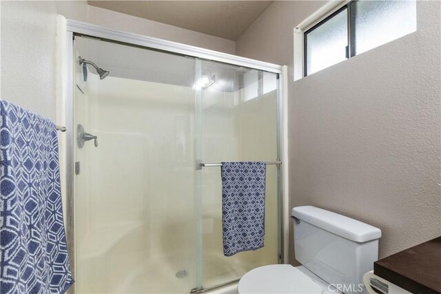 full bath with toilet, a textured wall, and a stall shower