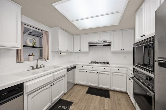 kitchen featuring white cabinets, a sink, under cabinet range hood, black appliances, and backsplash