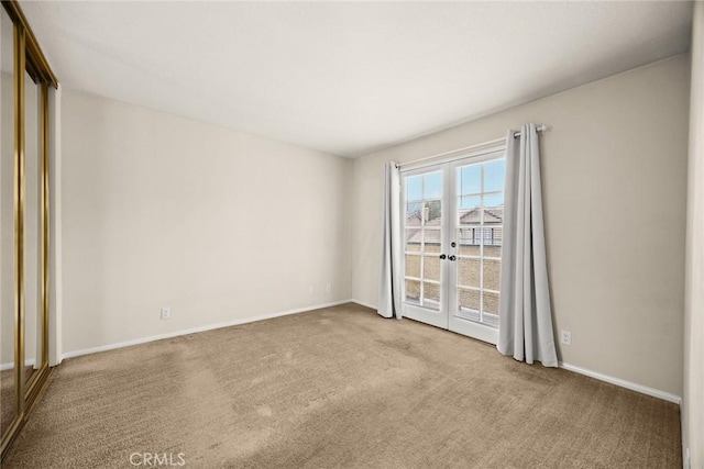 carpeted empty room featuring french doors and baseboards