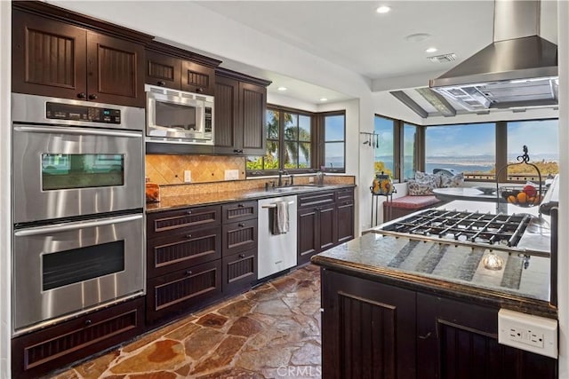 541 Via Del Monte, Palos Verdes Estates, CA 90274 - kitchen featuring stainless steel appliances, wall chimney range hood, dark brown cabinets, tasteful backsplash, and stone floors