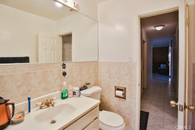bathroom featuring toilet, vanity, a wainscoted wall, and tile walls