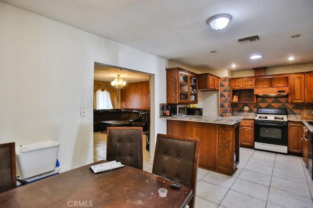 kitchen with range with gas stovetop, light tile patterned flooring, backsplash, a chandelier, and brown cabinetry