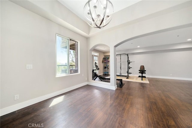 exercise area with baseboards, arched walkways, a notable chandelier, and dark wood finished floors
