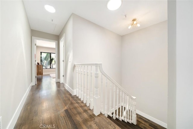 hall featuring dark wood-style flooring, an upstairs landing, and baseboards