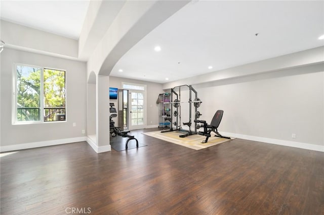 exercise room featuring dark wood-type flooring, arched walkways, baseboards, and recessed lighting