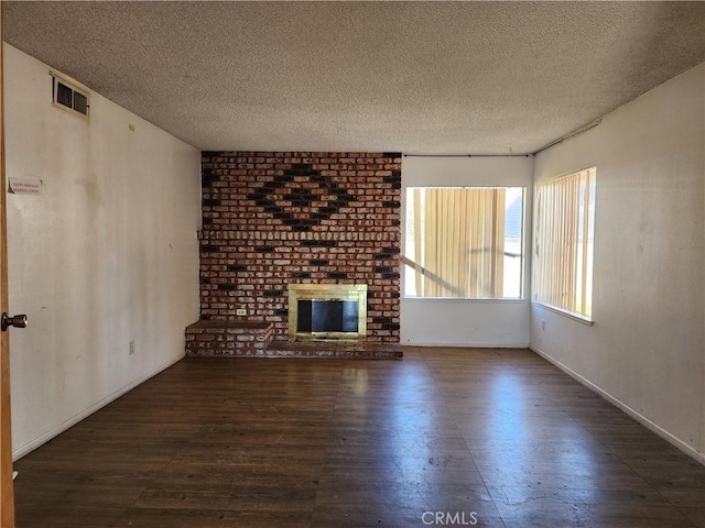 unfurnished living room featuring wood finished floors, a textured ceiling, a brick fireplace, baseboards, and visible vents