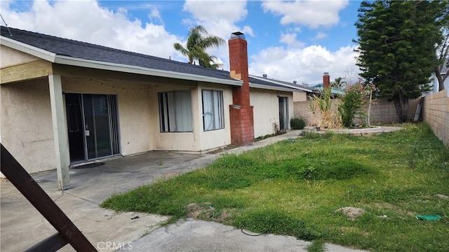 rear view of property featuring a patio, a chimney, a fenced backyard, stucco siding, and a yard