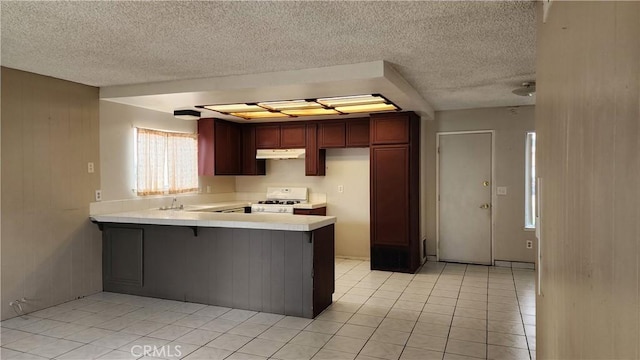 kitchen featuring light tile patterned flooring, range, light countertops, a peninsula, and under cabinet range hood