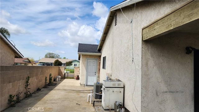 view of property exterior featuring a patio area, stucco siding, fence, and roof with shingles