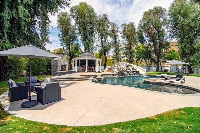view of swimming pool with fence, a water slide, a gazebo, an outdoor living space with a fireplace, and a patio area