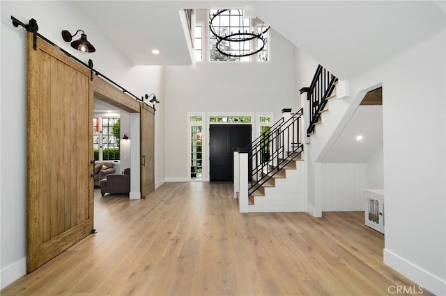 entrance foyer featuring stairs, a notable chandelier, a barn door, baseboards, and light wood-style floors