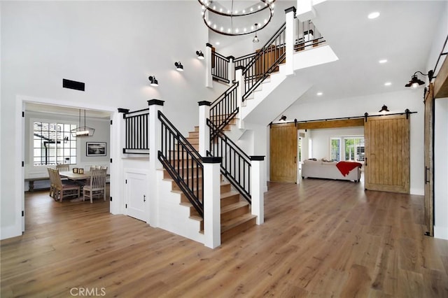 stairs with a high ceiling, a barn door, wood finished floors, and an inviting chandelier