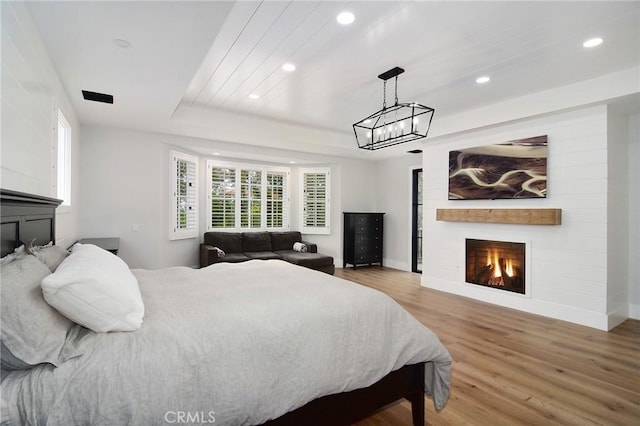 bedroom featuring a raised ceiling, wood finished floors, a large fireplace, baseboards, and recessed lighting