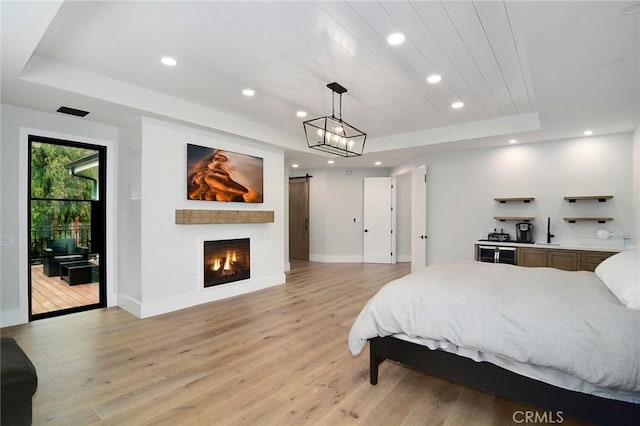 bedroom with light wood-style flooring, a tray ceiling, recessed lighting, and wet bar