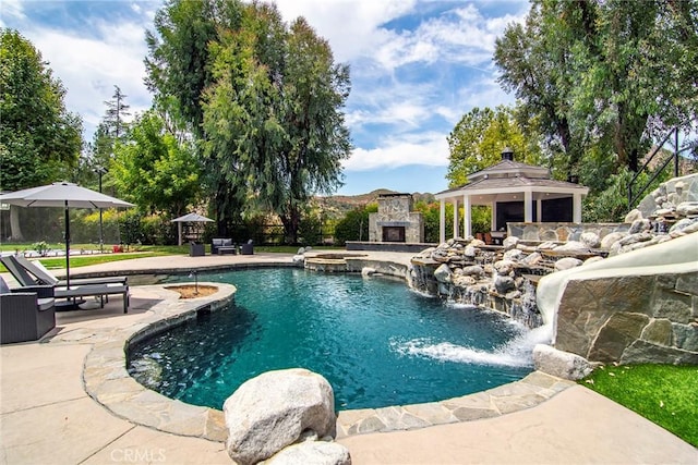 view of pool featuring a pool with connected hot tub, a gazebo, an outdoor stone fireplace, and a patio