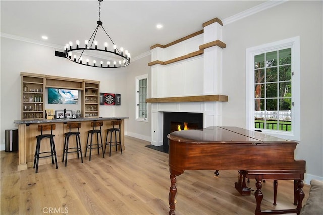 dining area featuring a notable chandelier, crown molding, a fireplace with flush hearth, light wood-type flooring, and baseboards