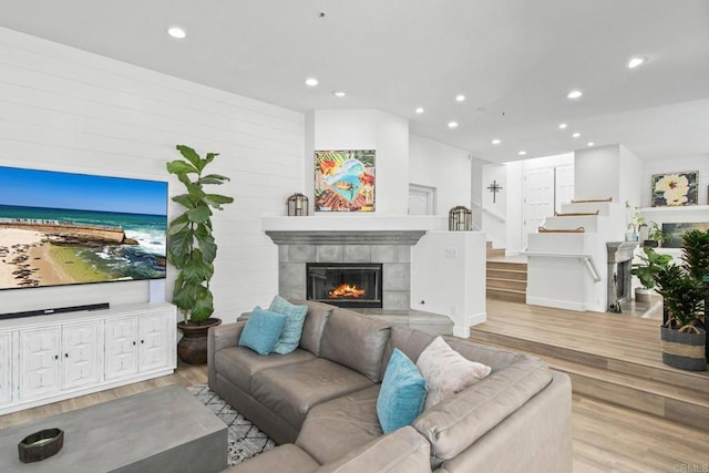 living area with stairway, recessed lighting, a tile fireplace, and wood finished floors