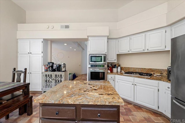 4981 Marin Dr, Oceanside, CA 92056 - kitchen with visible vents, a center island, white cabinets, light stone counters, and appliances with stainless steel finishes