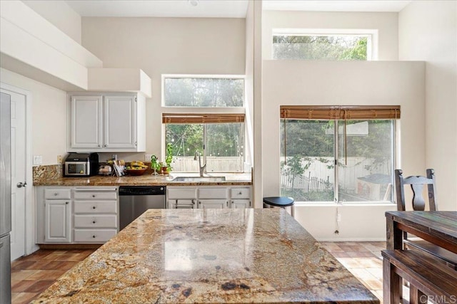 4981 Marin Dr, Oceanside, CA 92056 - kitchen featuring stainless steel dishwasher, light stone counters, a towering ceiling, healthy amount of natural light, and white cabinets