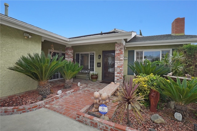 entrance to property with a chimney, stucco siding, and covered porch