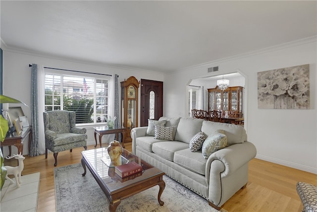 living room featuring ornamental molding, arched walkways, light wood finished floors, visible vents, and a notable chandelier
