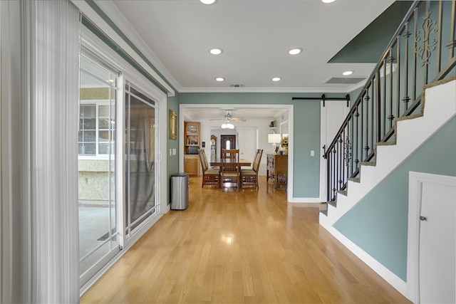 foyer featuring a barn door, light wood-type flooring, stairs, and crown molding
