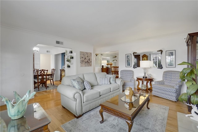 living room featuring light wood-type flooring, ornamental molding, arched walkways, visible vents, and a notable chandelier