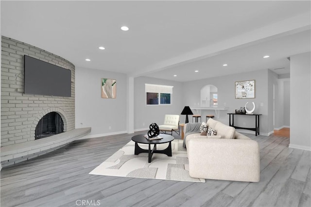 living room with wood finished floors, baseboards, a brick fireplace, and recessed lighting